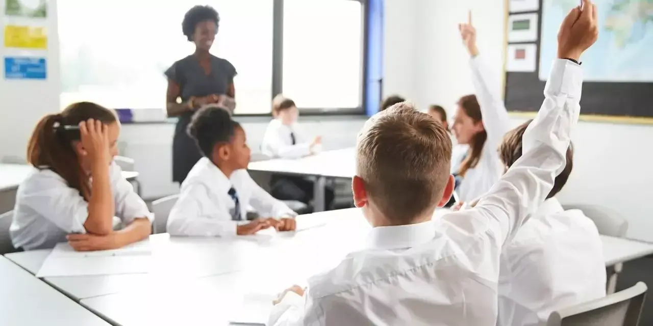 students sat in a class with two of them holding their hands up to answer a question