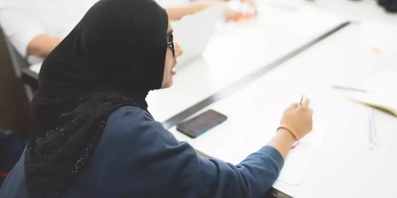 a student in a hijab writing at a desk