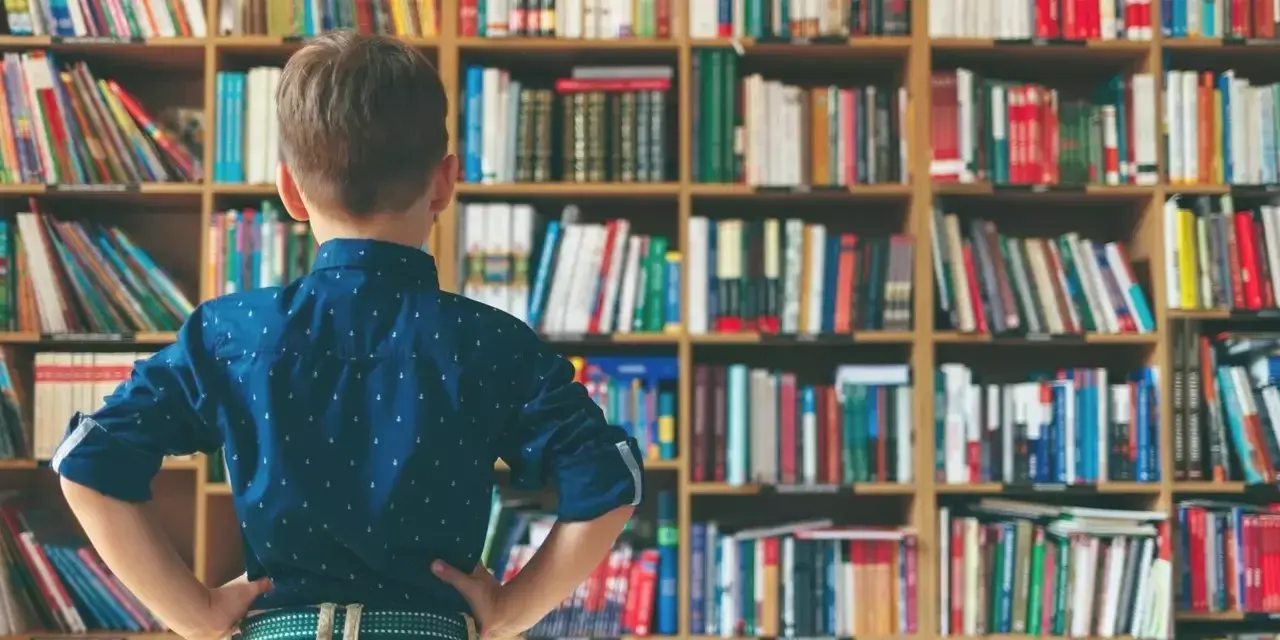 a boy with his hands on his hips in the library trying to decide what to read