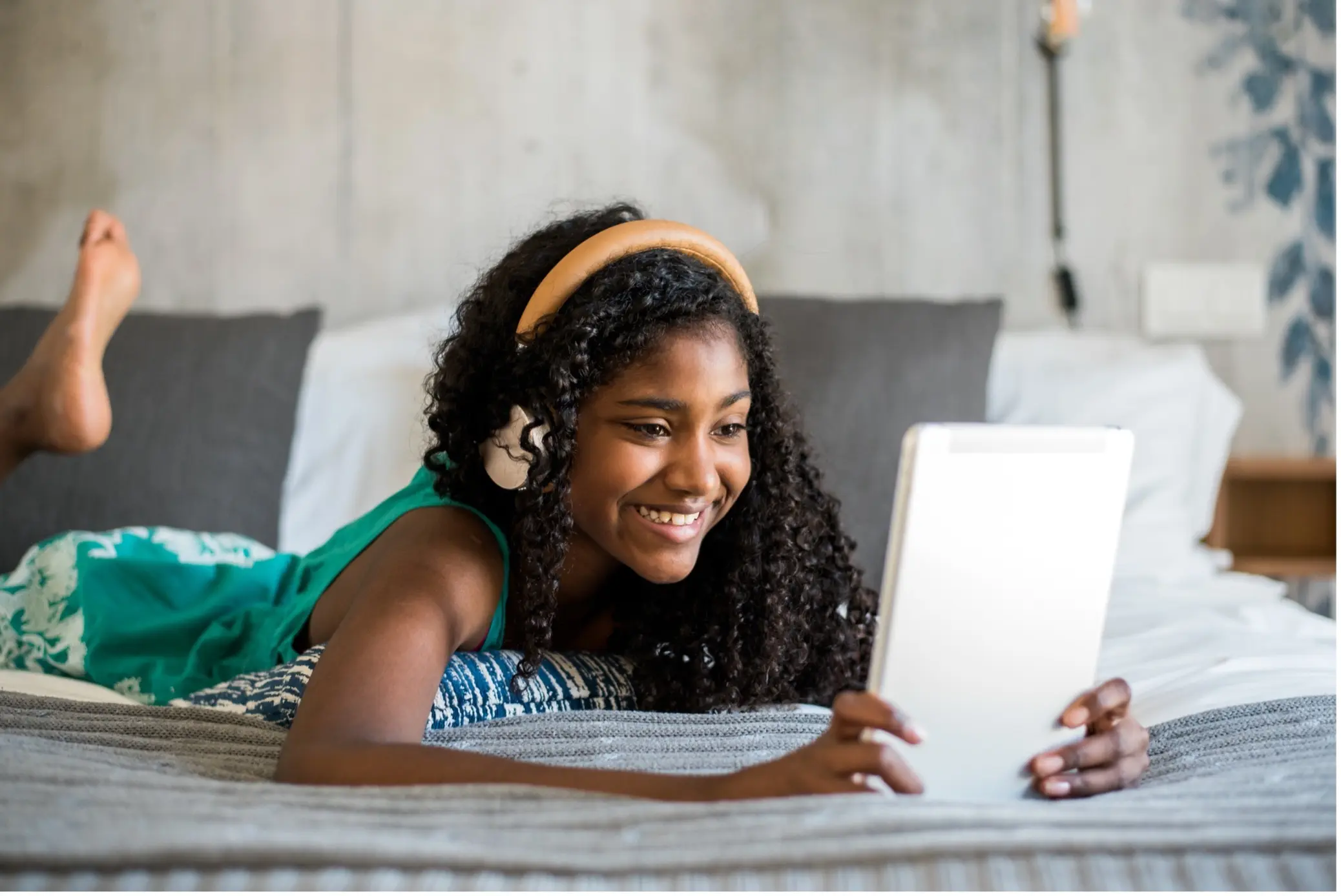 a teenage girl laid on a bed wearing headphones reading on a tablet