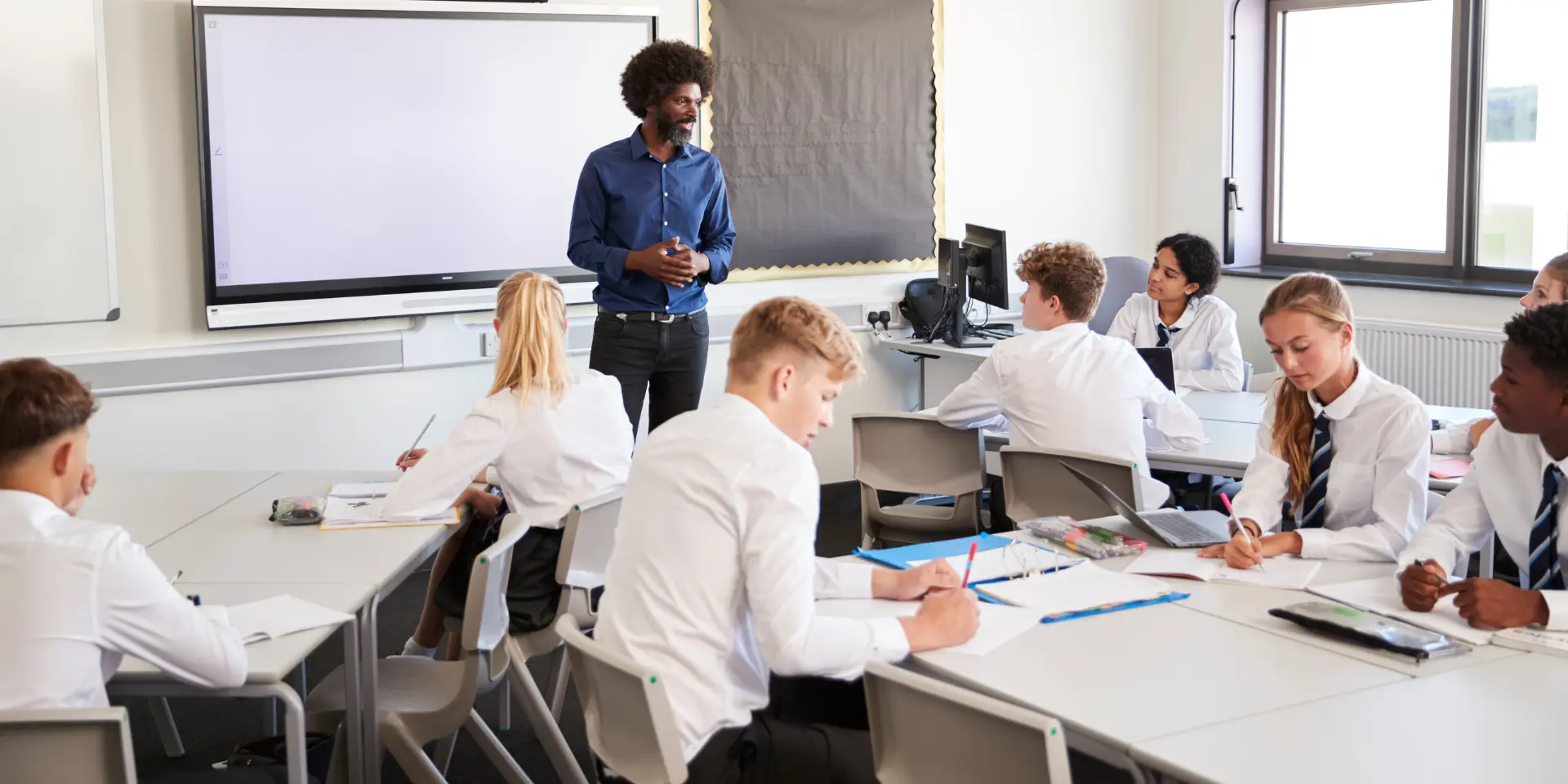 Male High School Teacher Standing Next To Interactive Whiteboard And Teaching