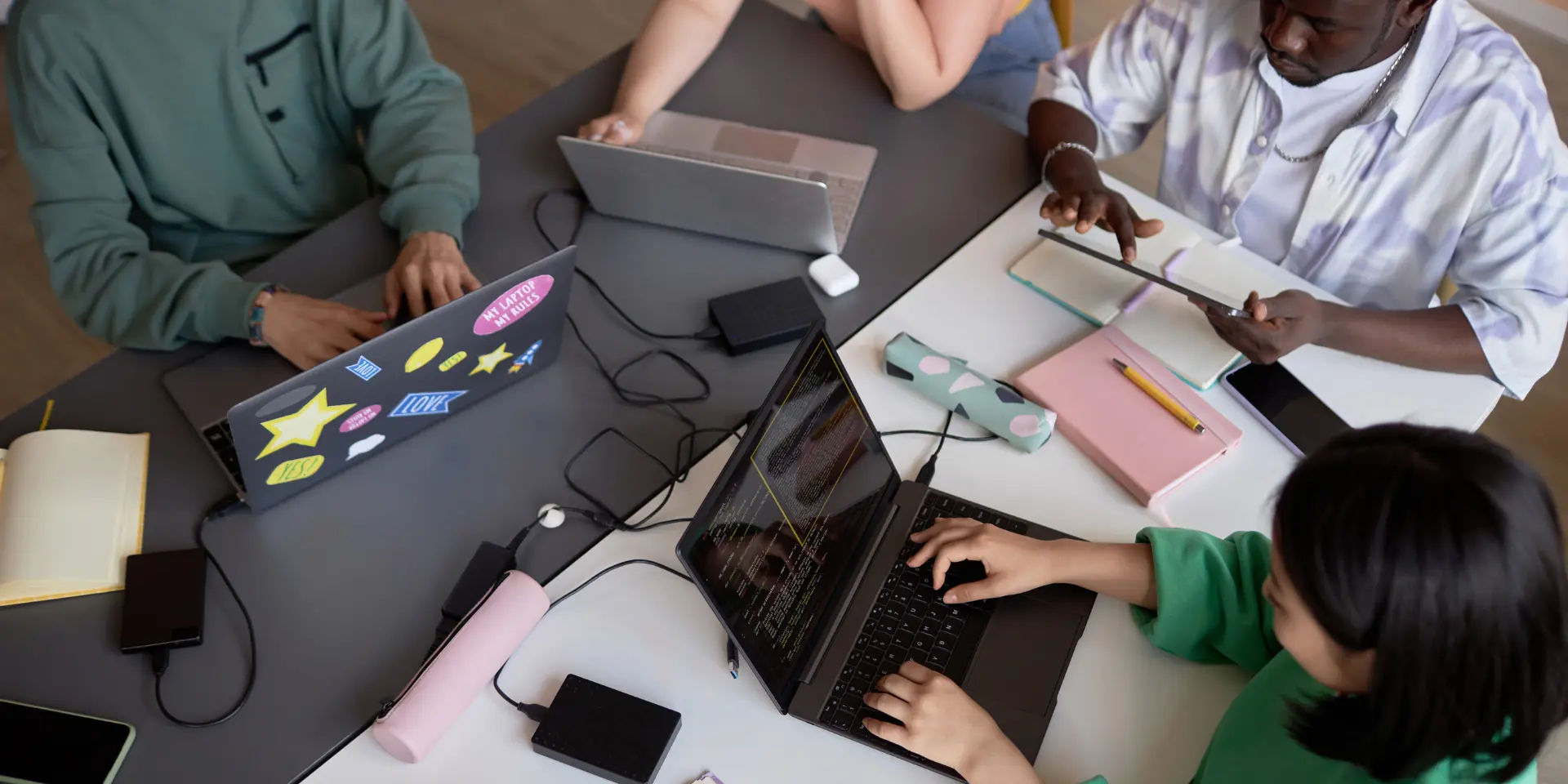 Above angle of team of young students sitting by table and using mobile gadgets