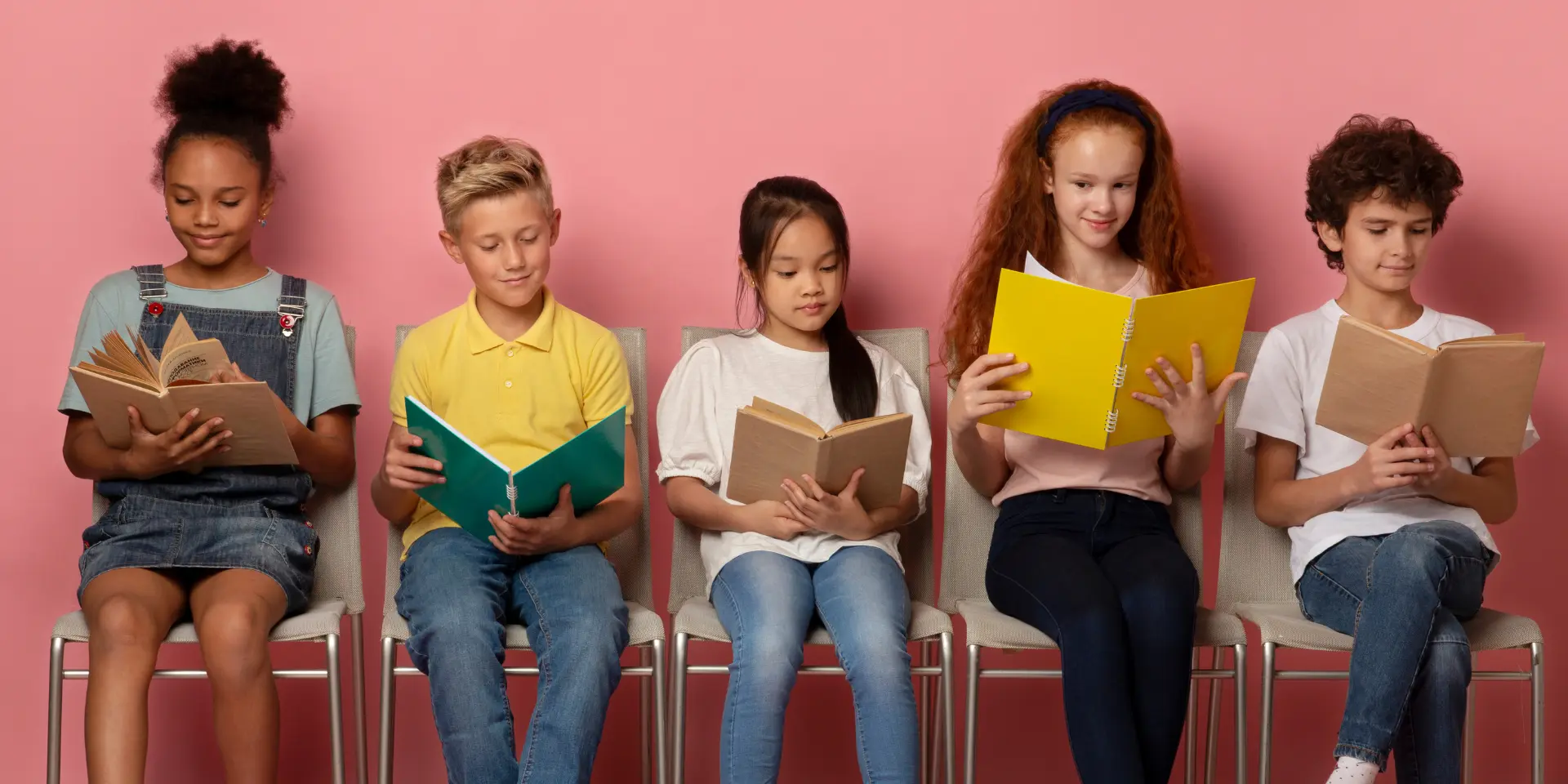 Diverse kids with textbooks and notebooks sitting on chairs getting ready for school lesson on pink