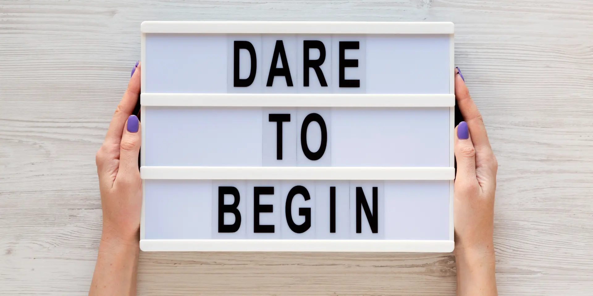 Female hands hold lightbox with Dare to begin words over white wooden surface top view