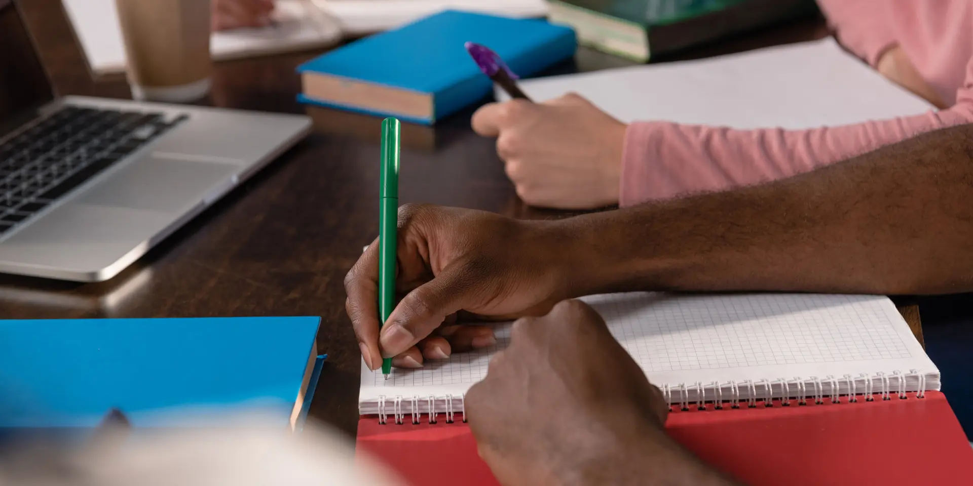 Cropped view of students studying and writing in copybooks together at home