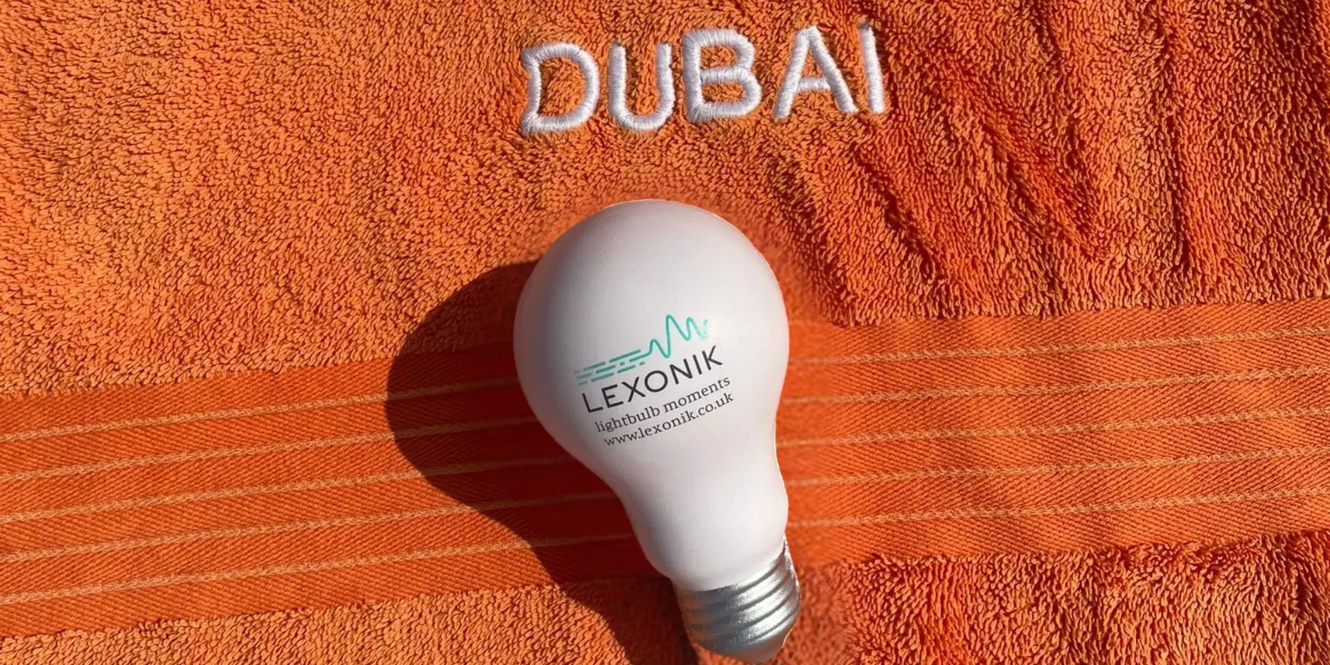 an orange towel laid on a beach in dubai with a lightbulb showing the lexonik logo atop it