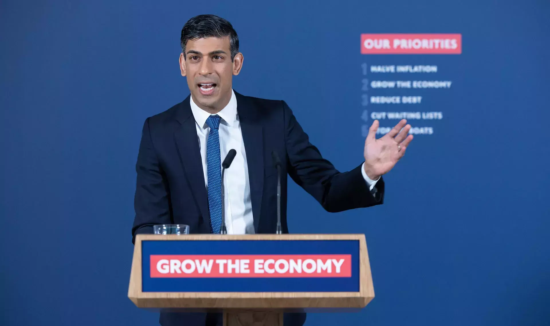 rishi sunak in front of a podium that reads 'grow the economy' giving a speech