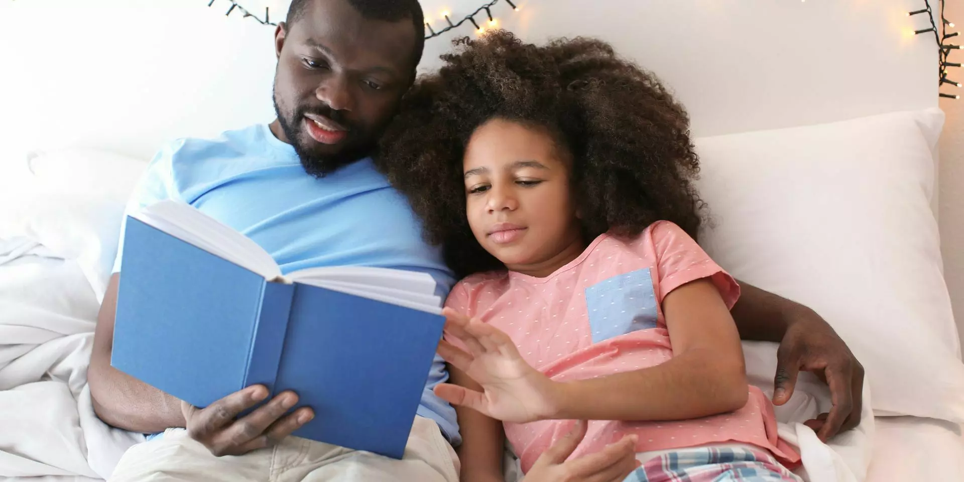 a farther and daughter in a bed reading together