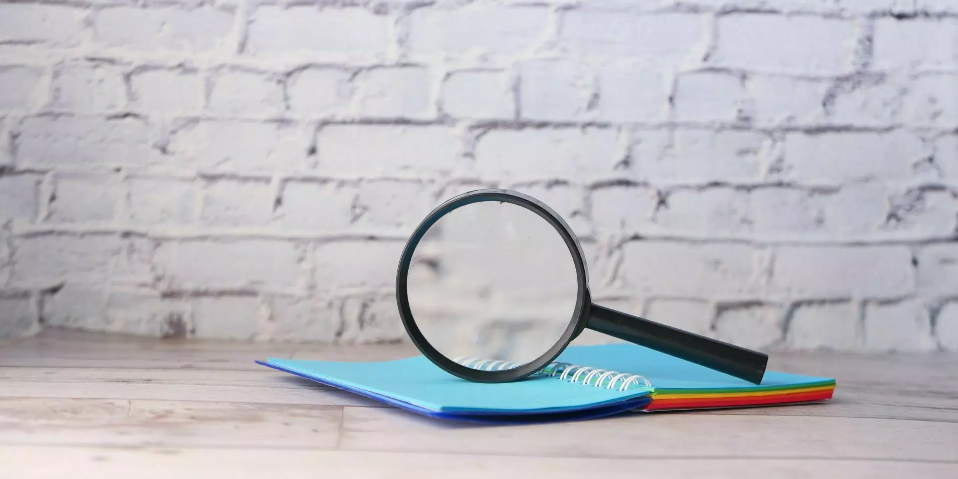a magnifying glass on top of a notebook against a white brick wall