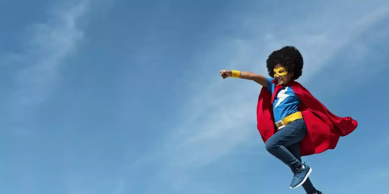a child dressed as a superhero jumping into the air with the clouds in the background