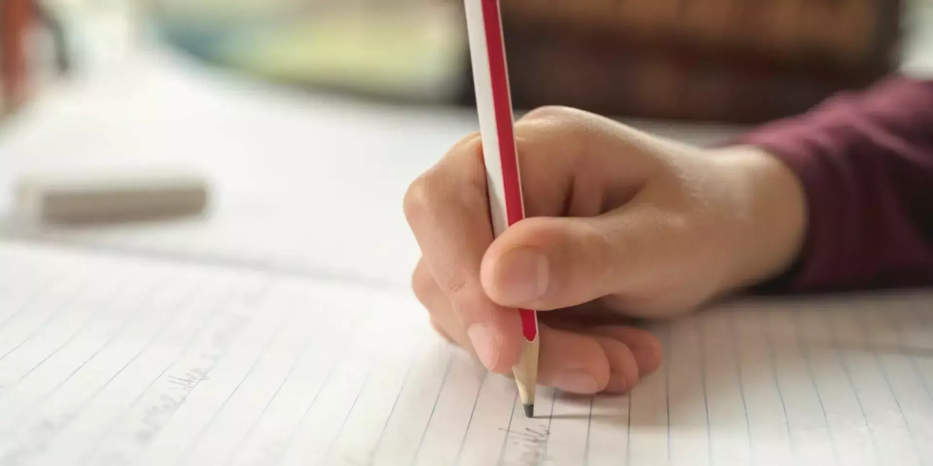 a child writing on a sheet of paper with a pencil