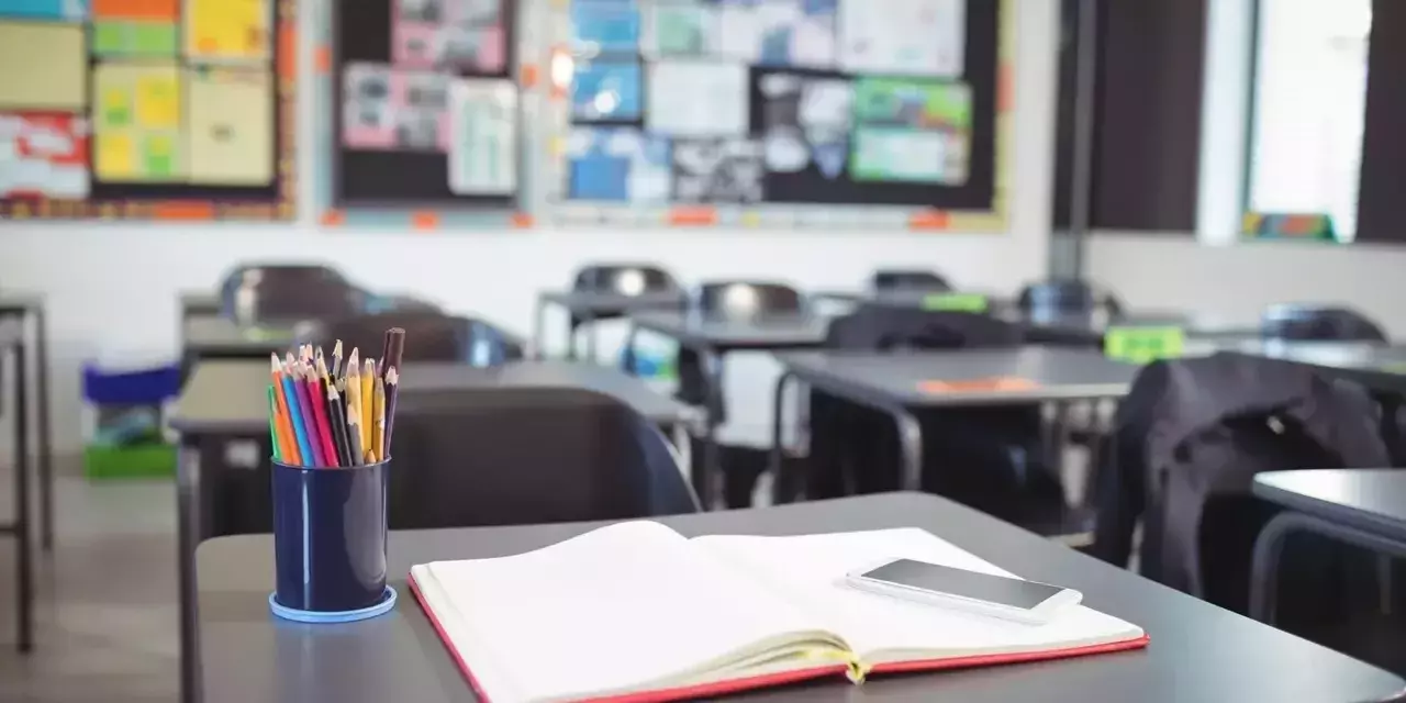 a desk with an open notebook a phone and a pot of pencils on top of it