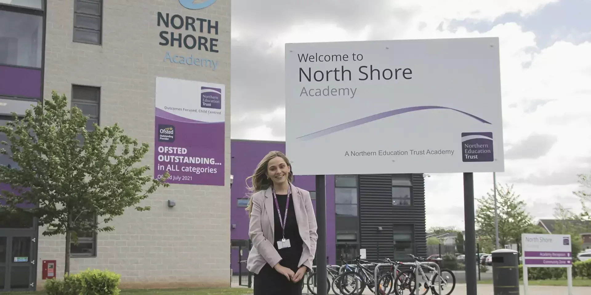 a teacher stood in front of the entrance sign to north shore academy